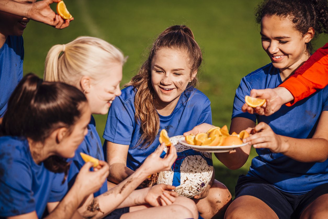 A young athlete laughing with teammates while they share fruit after training