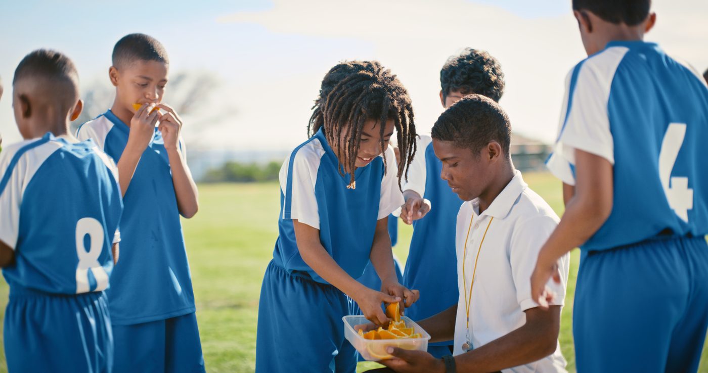 A youth soccer team sharing fruit together at the side of the pitch